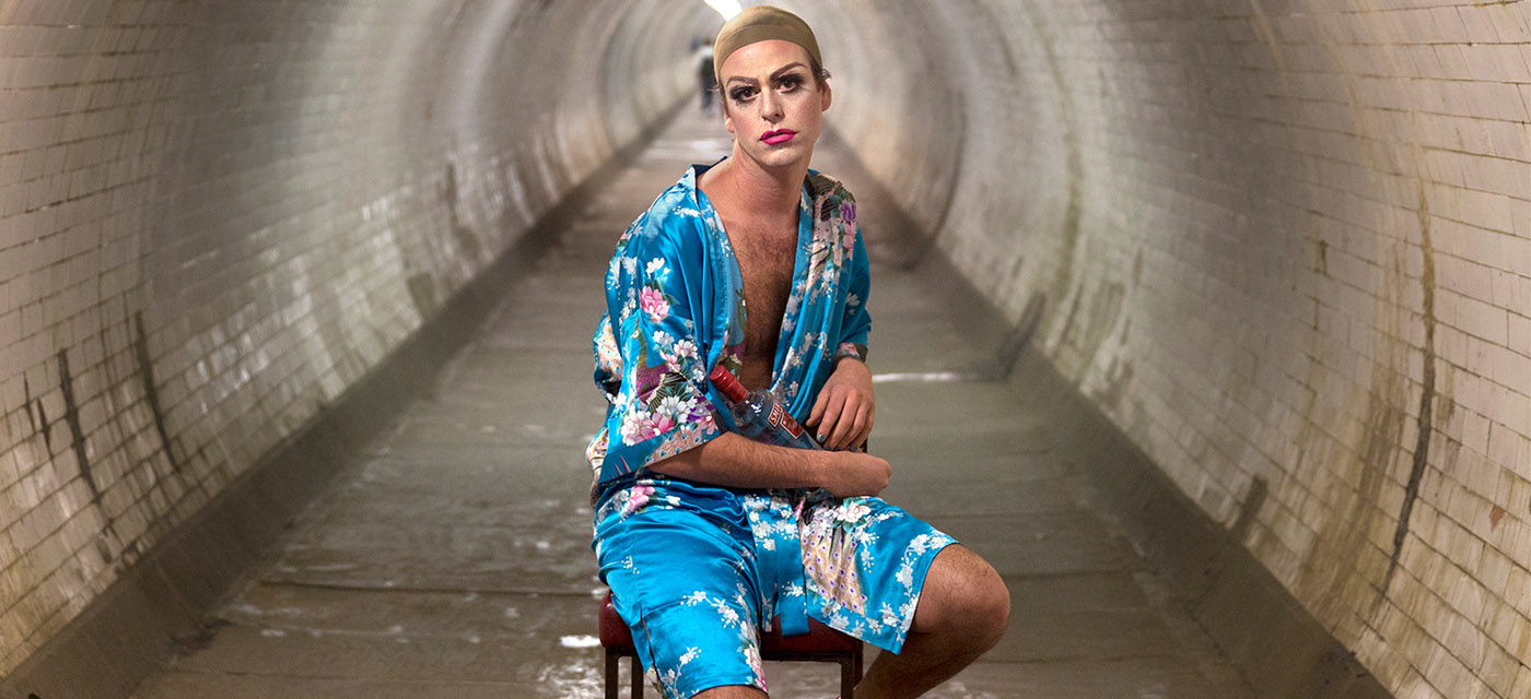 A seated performer in a tunnel looking into the camera