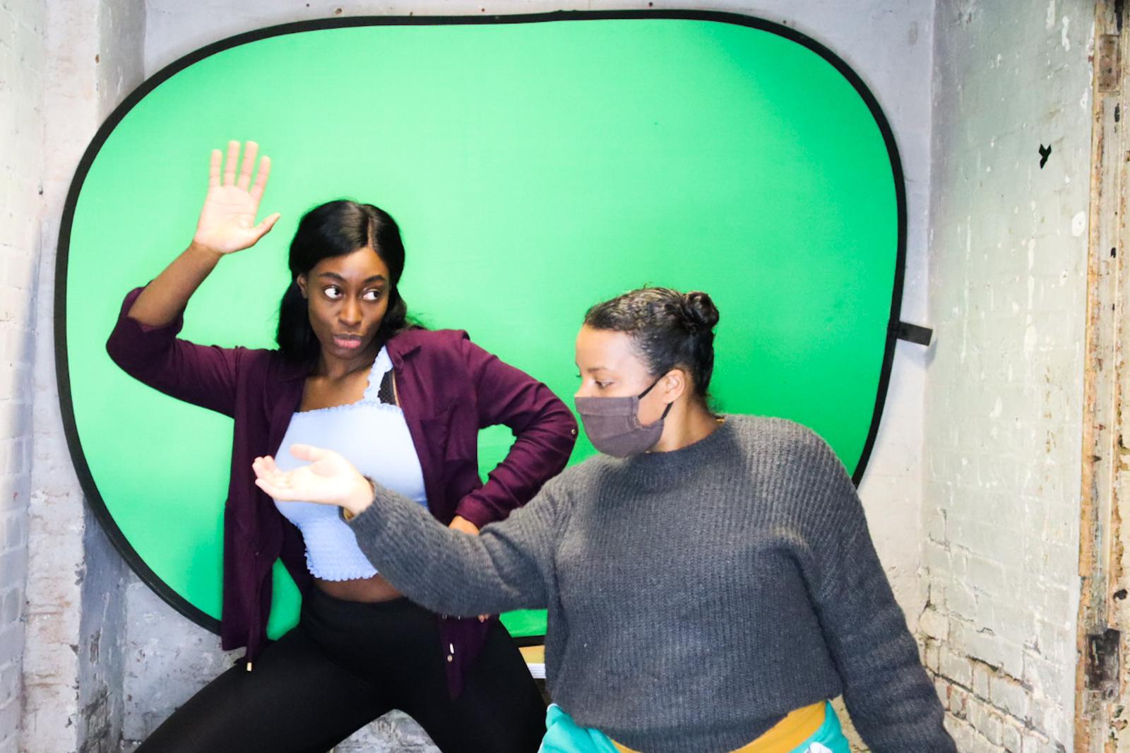 Two performers gesturing in front of a green screen.
