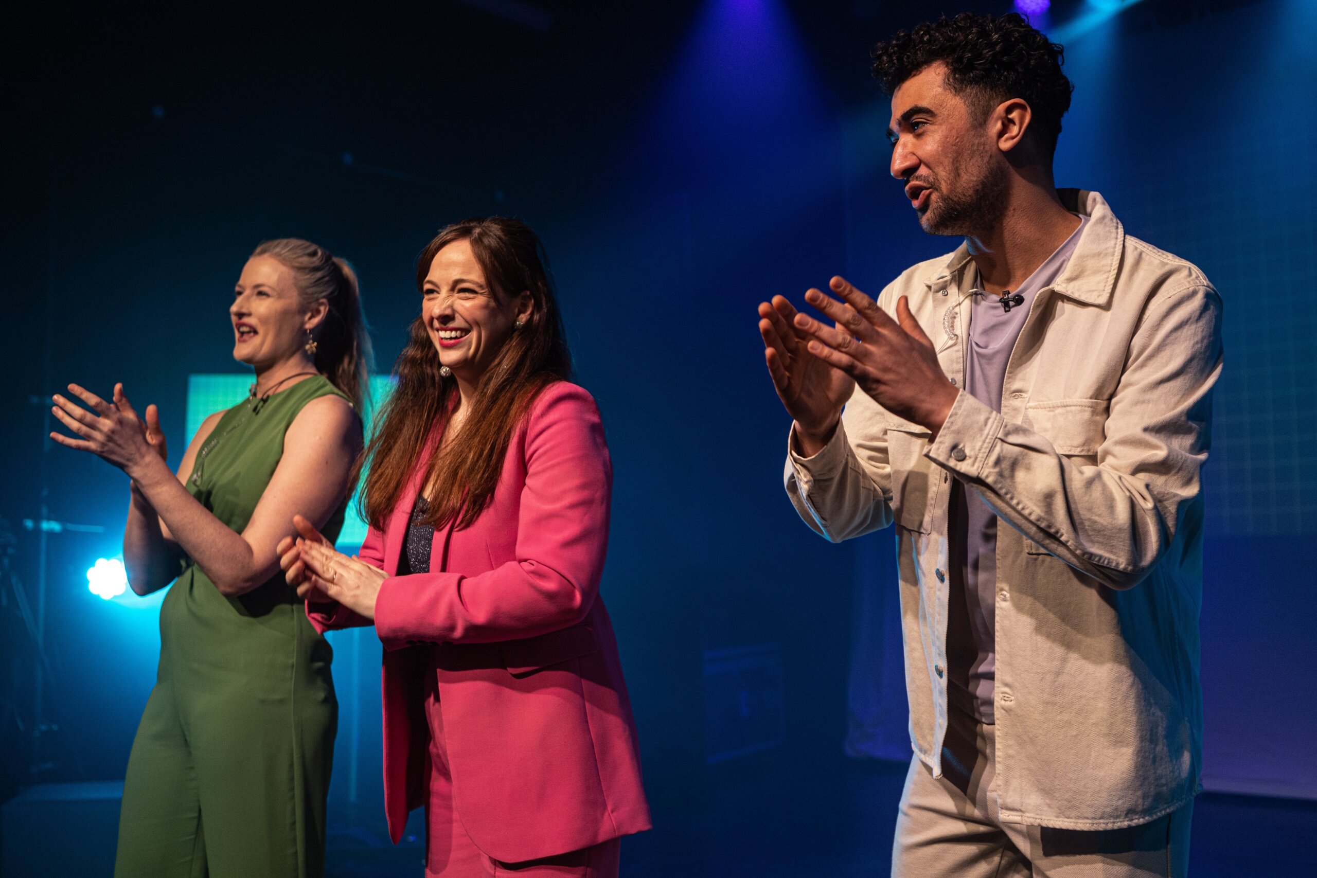 three people stand on a stage, applauding and laughing