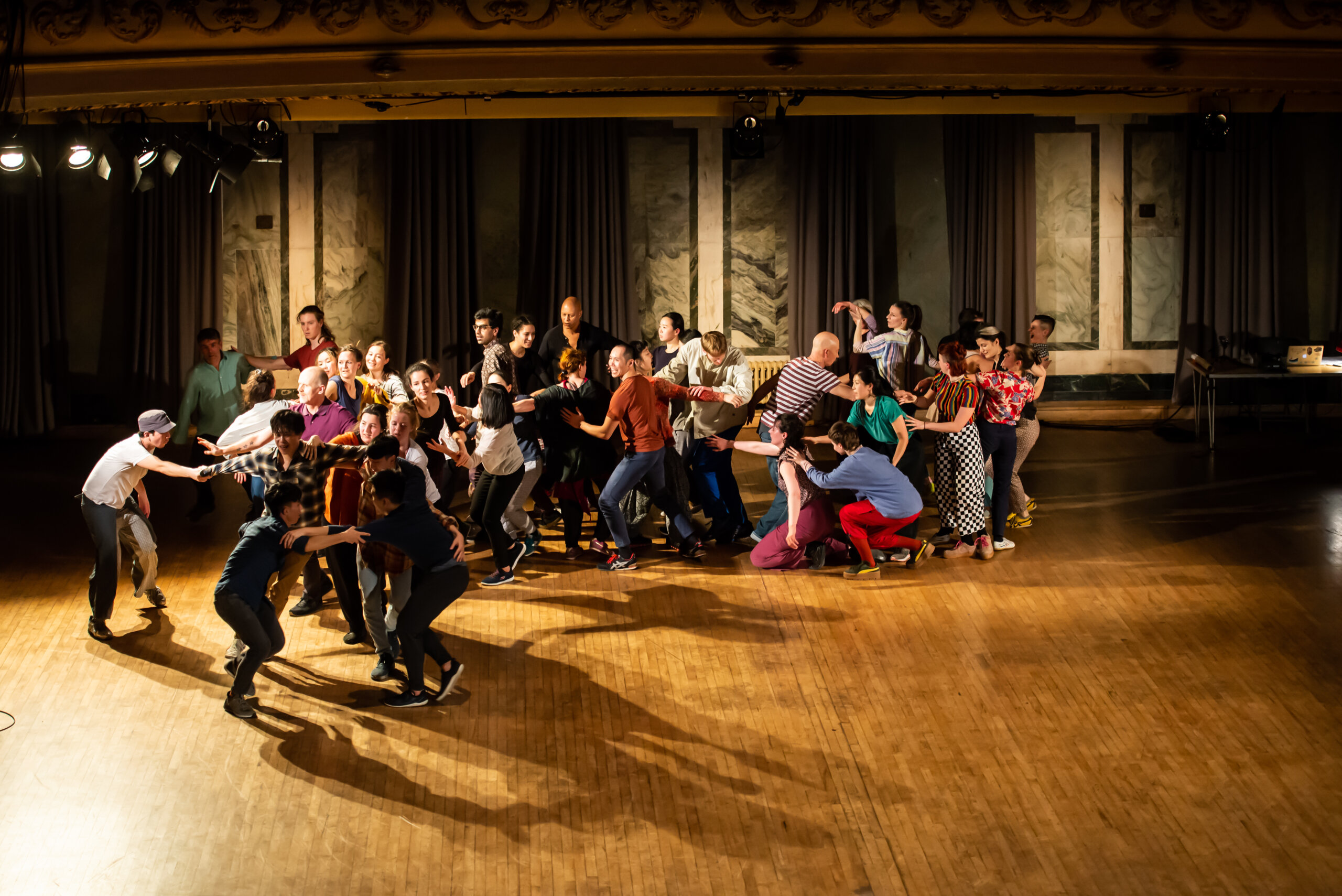 A group of dancers moving collectively across a room in an animated fashion